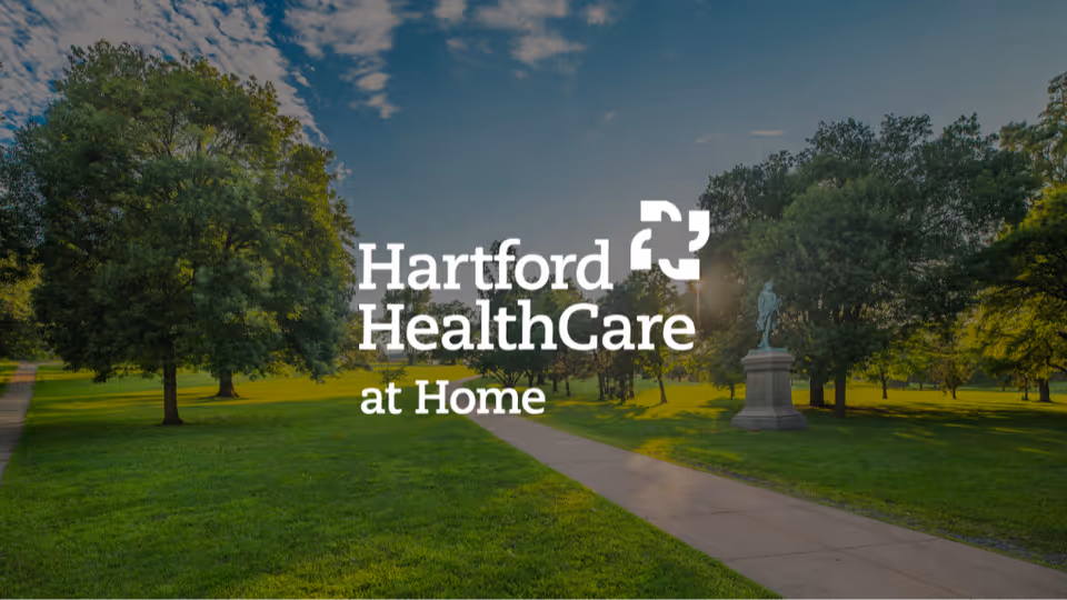 A park-like outdoor area with a path, trees, and a Hartford HealthCare at Home logo.