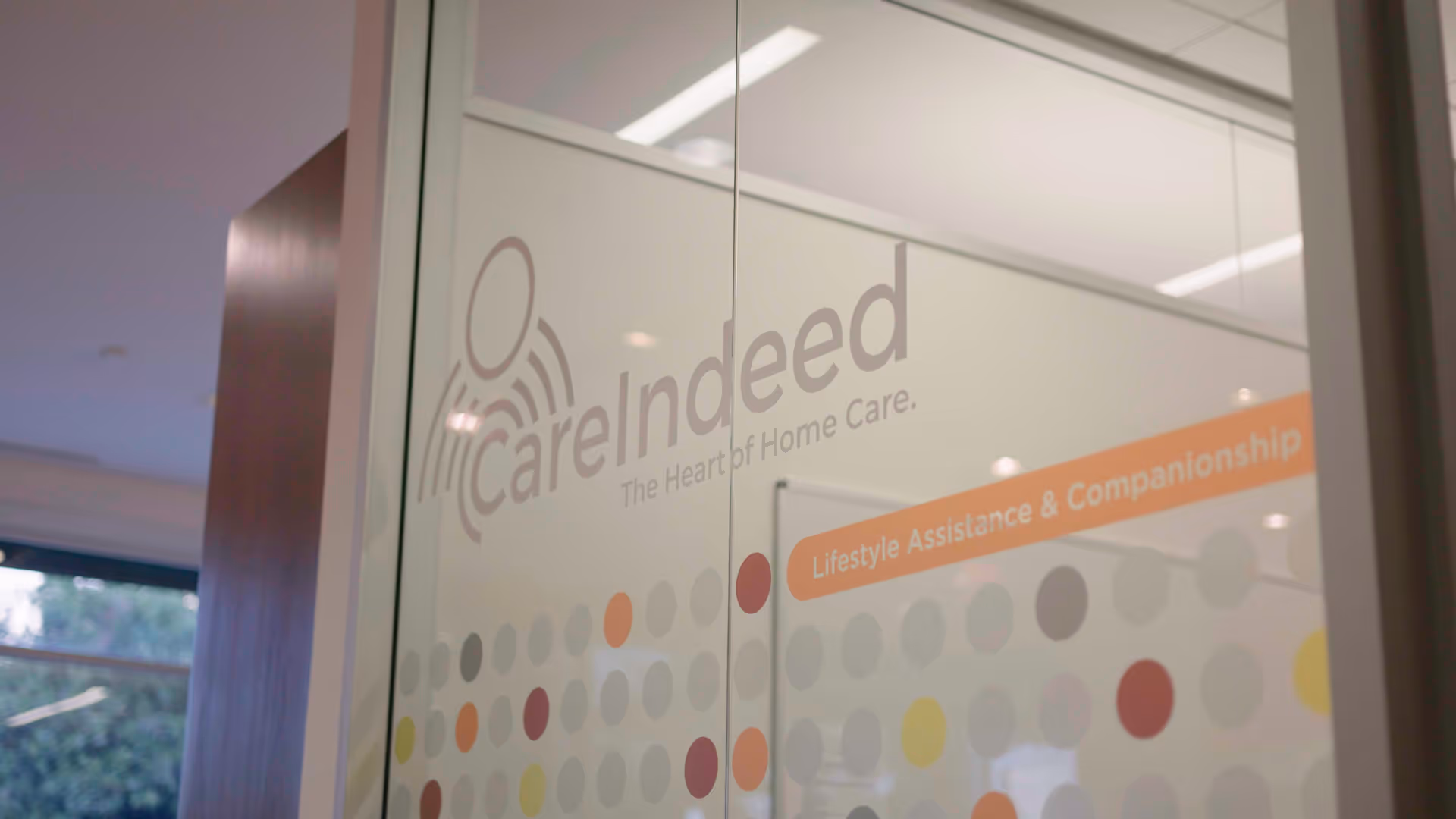 Glass door displaying Care Indeed logo and lifestyle assistance banner inside the facility.