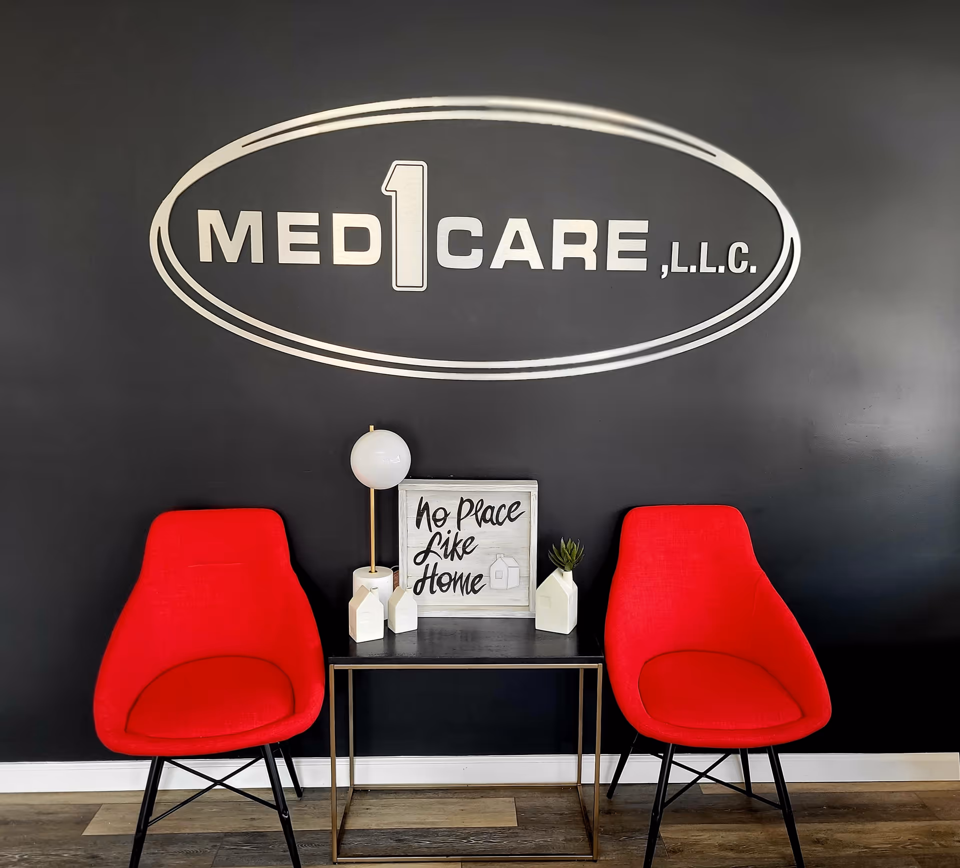 Interior lobby area with black wall, Med1Care logo, red chairs, and a small table.