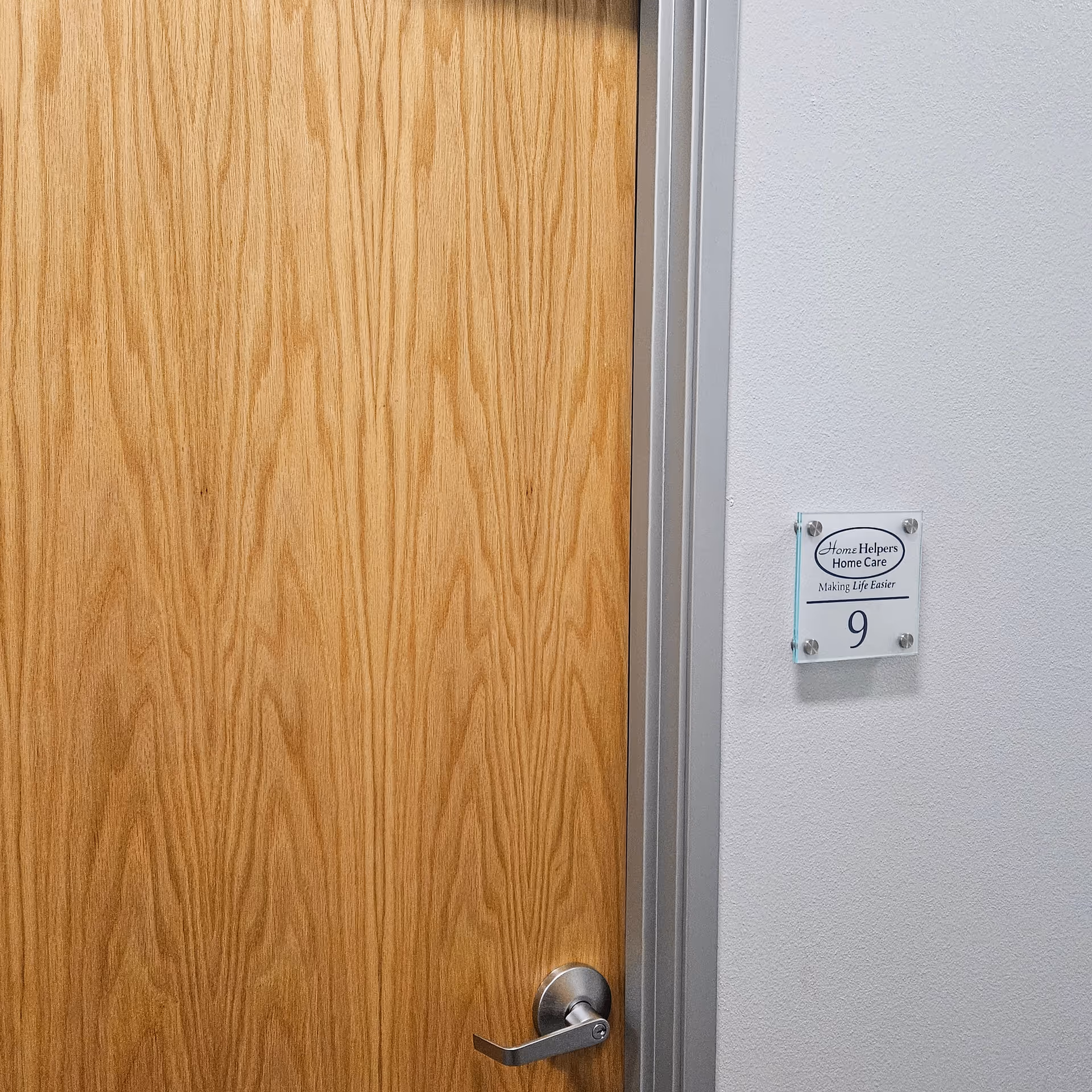 A wooden door in a hallway with a plaque labeled Home Helpers, room 9.