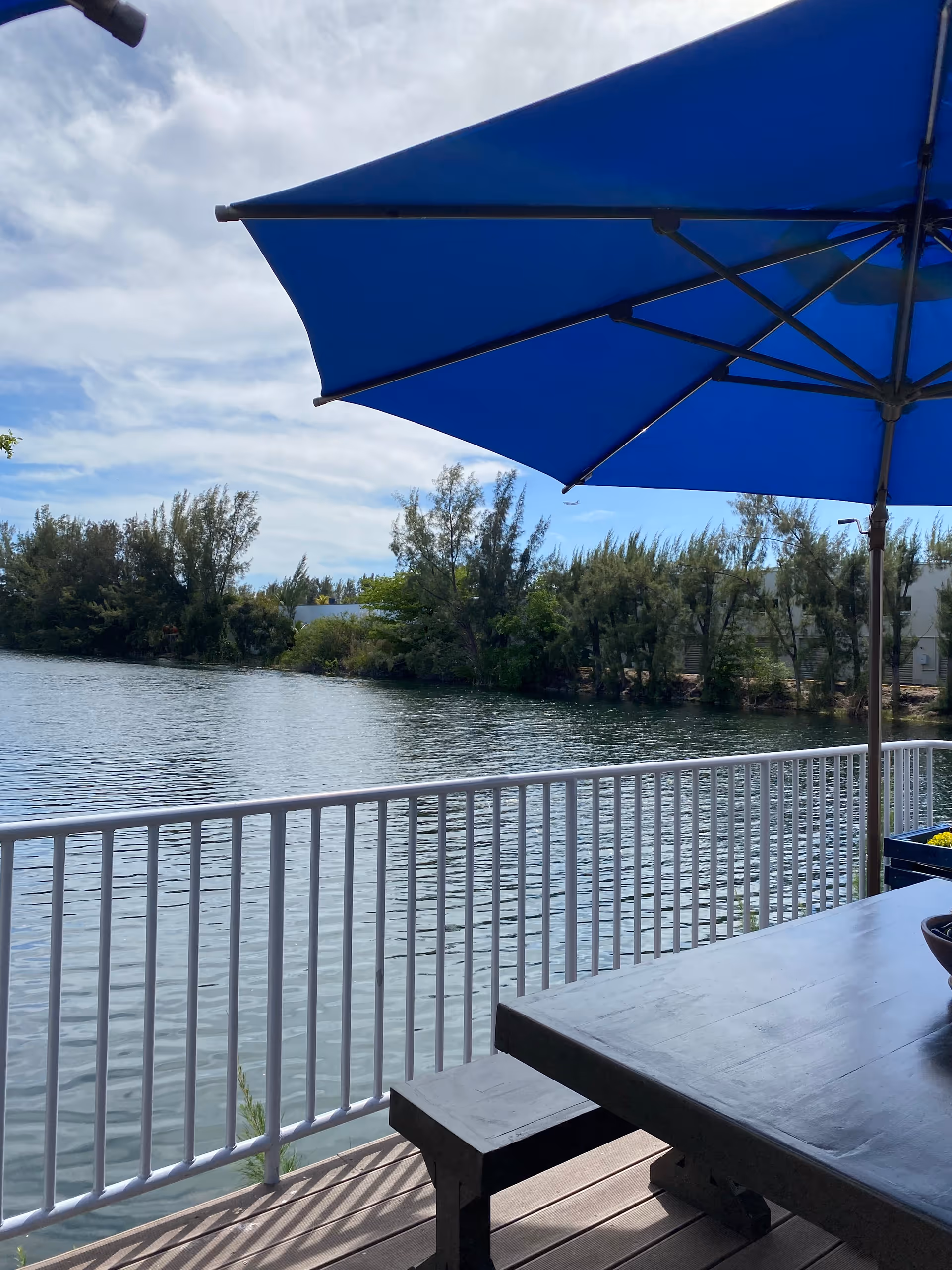 Outdoor patio with a blue umbrella beside a railing overlooking calm water.