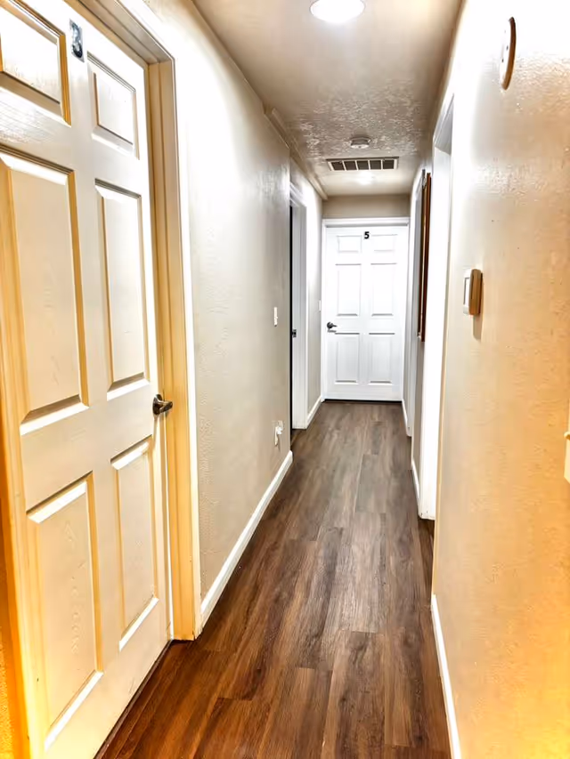 Narrow hallway in a senior living facility with white doors and wood laminate flooring.