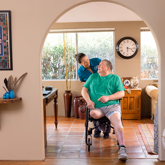 Caregiver assists a man in a wheelchair in a cozy living room.
