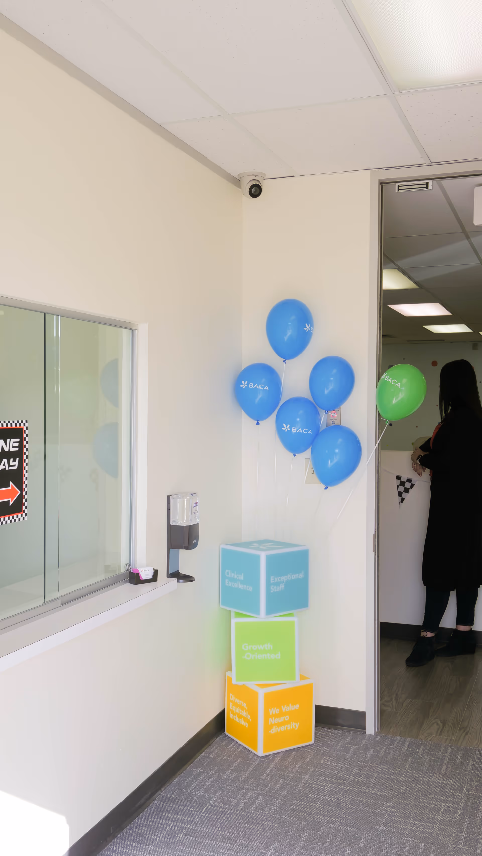 Interior hallway with blue balloons, stacked colorful cubes, window counter, and a person near the doorway.