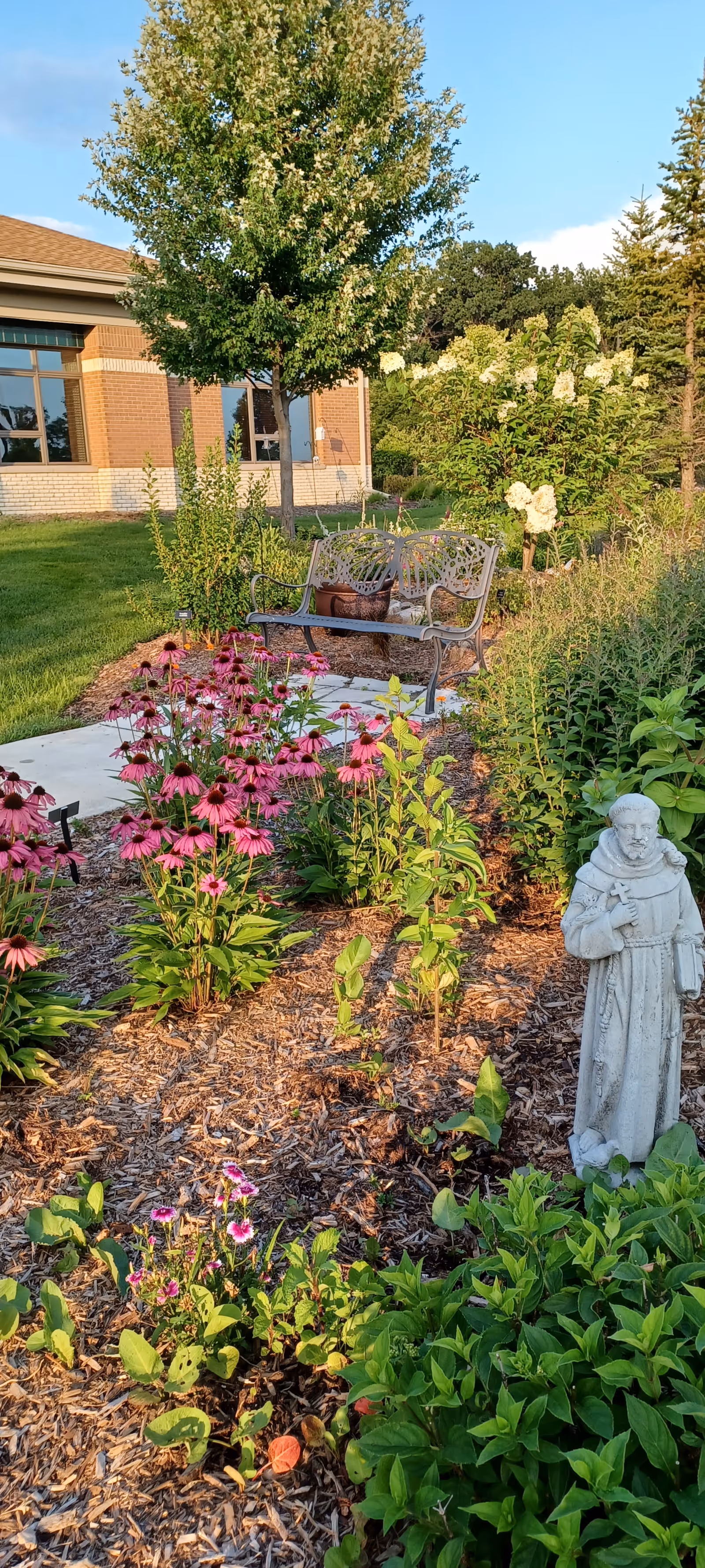 Angela Hospice garden with a bench, flowers, statue, and building in the background.