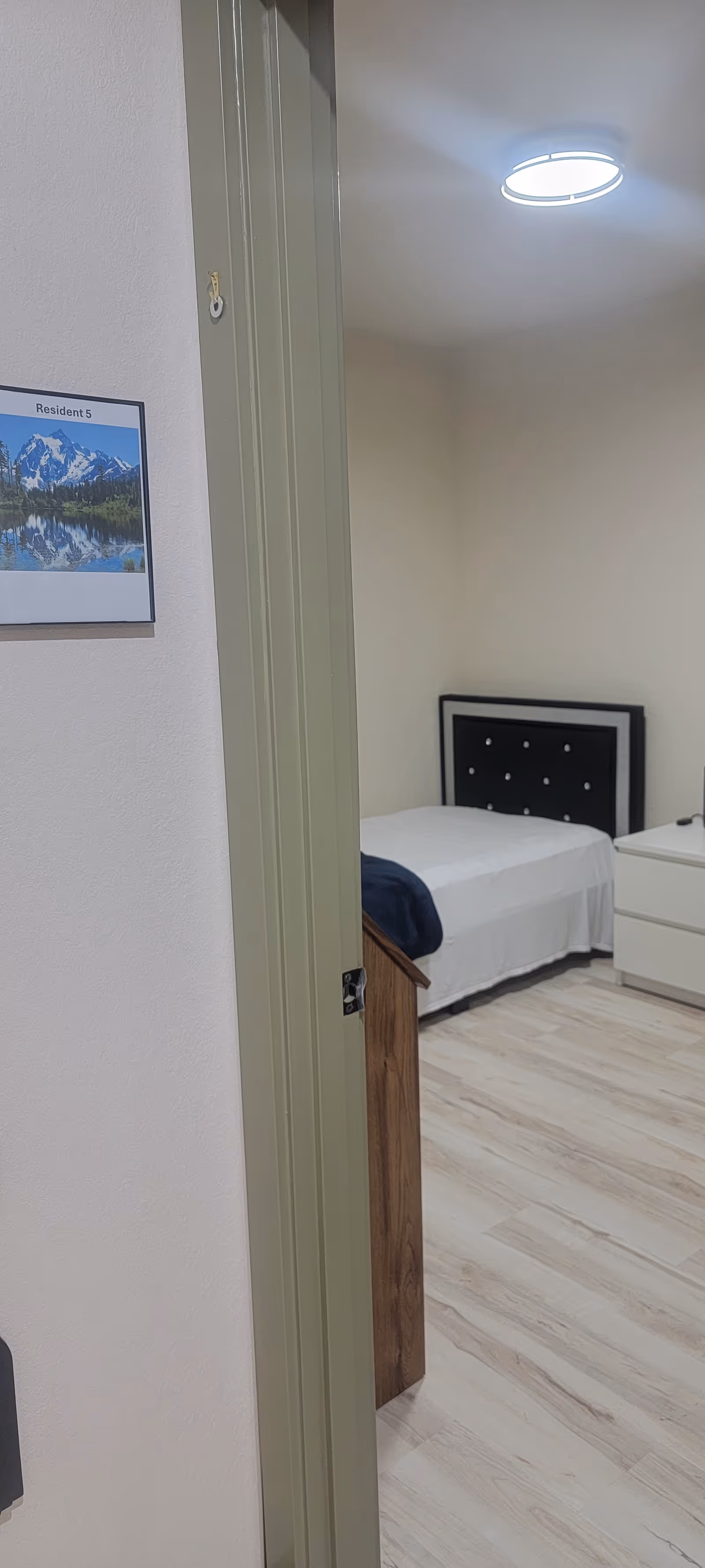 A tidy bedroom in a senior living facility with a bed, nightstand, and dresser.
