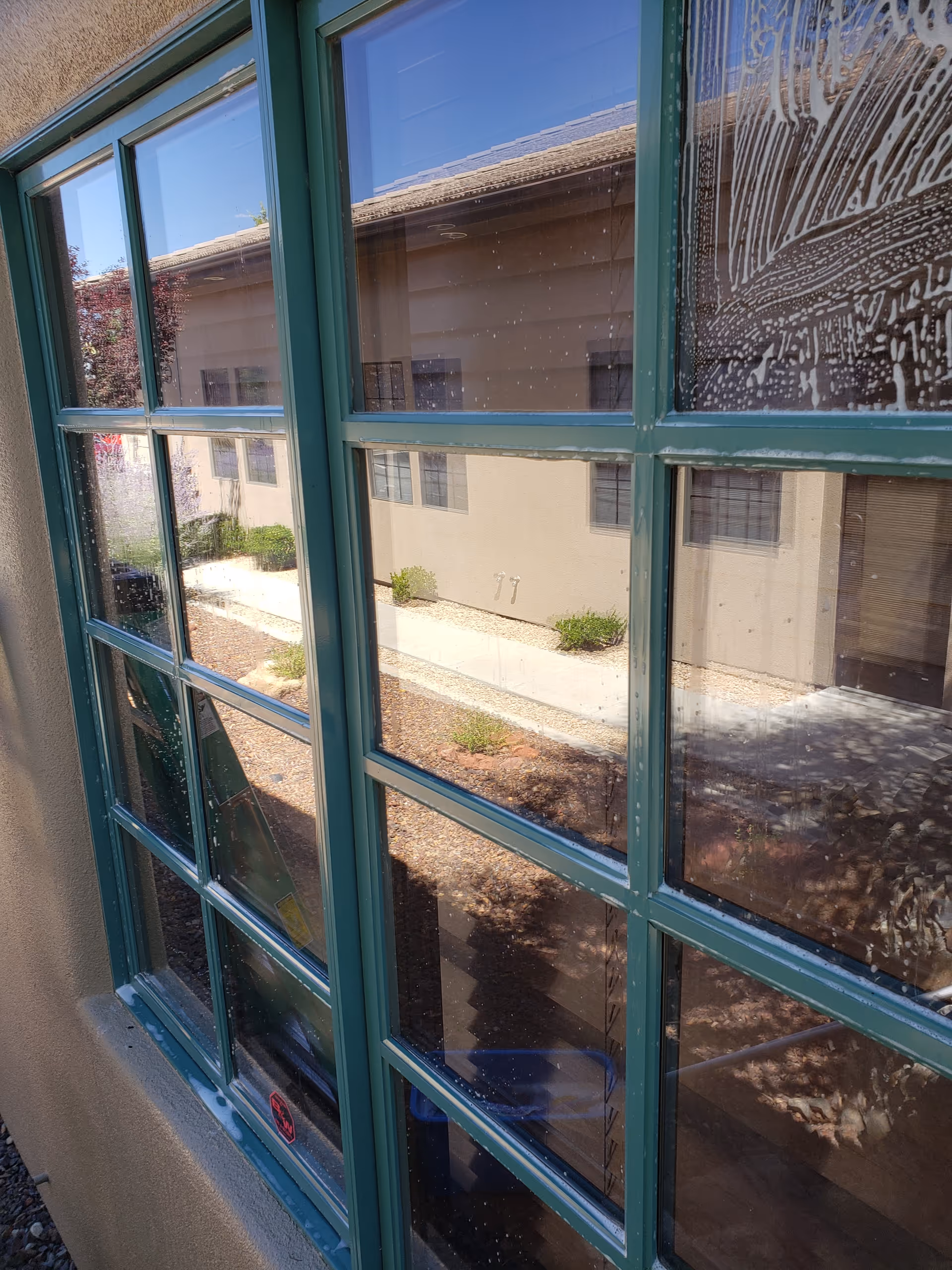 Green-framed windows overlook a beige building and small courtyard with shrubs.