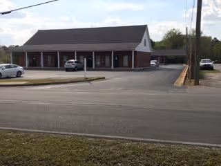 Single-story brick building with a covered front porch and a parking lot.