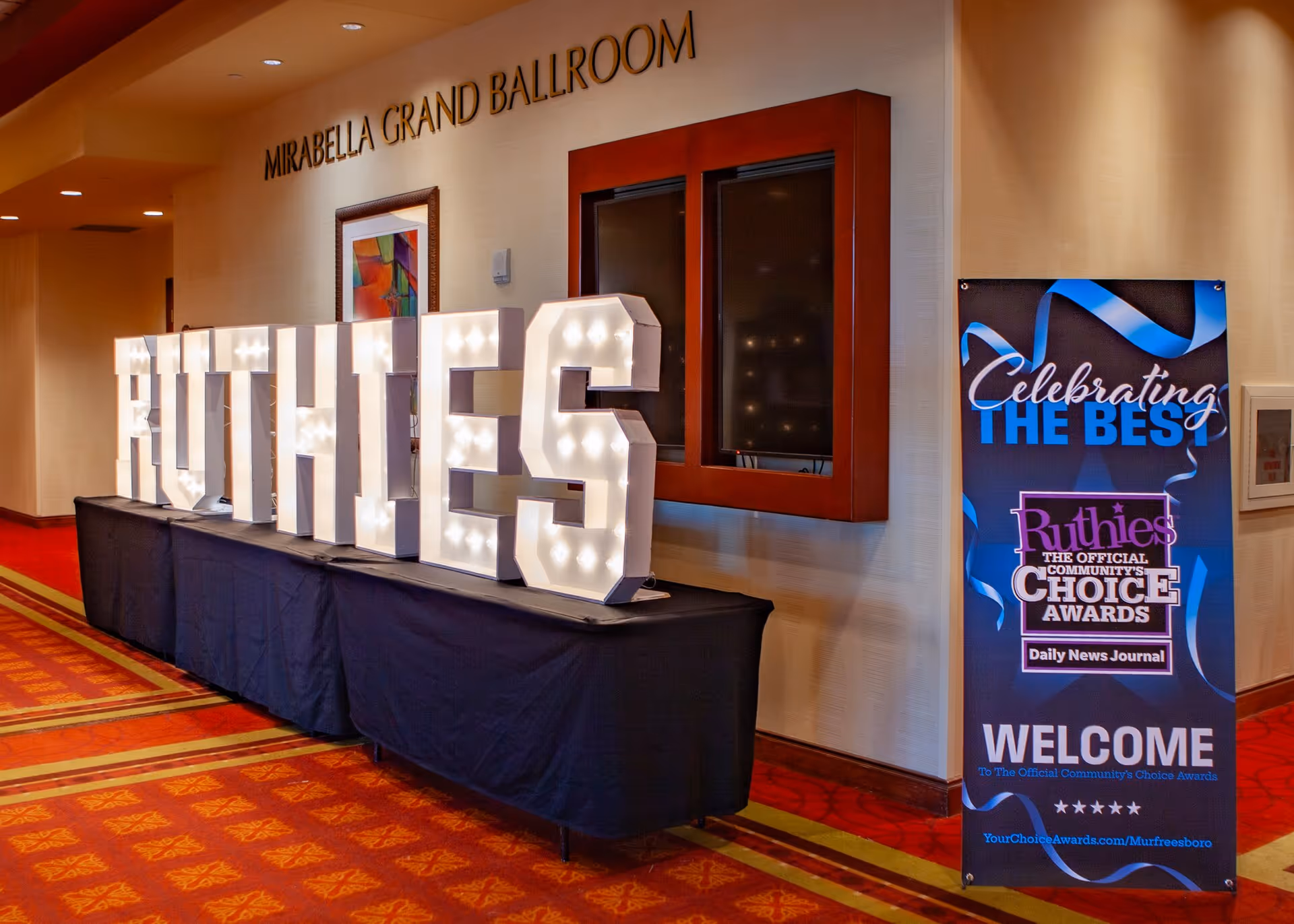 Illuminated Ruthies letters on a table in a ballroom lobby with a welcome banner.