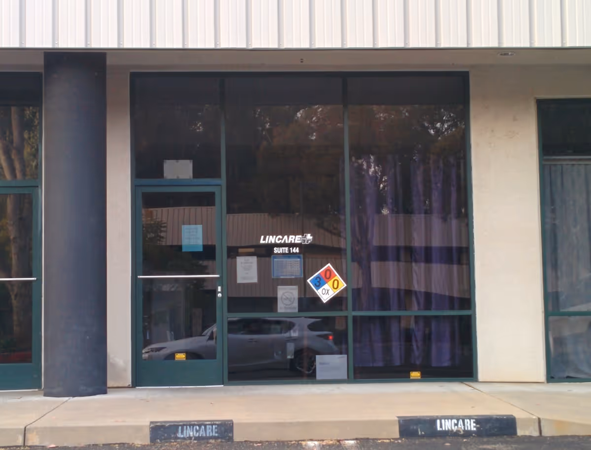 Front entrance of a LINCARE facility with glass doors and a hazard sign.