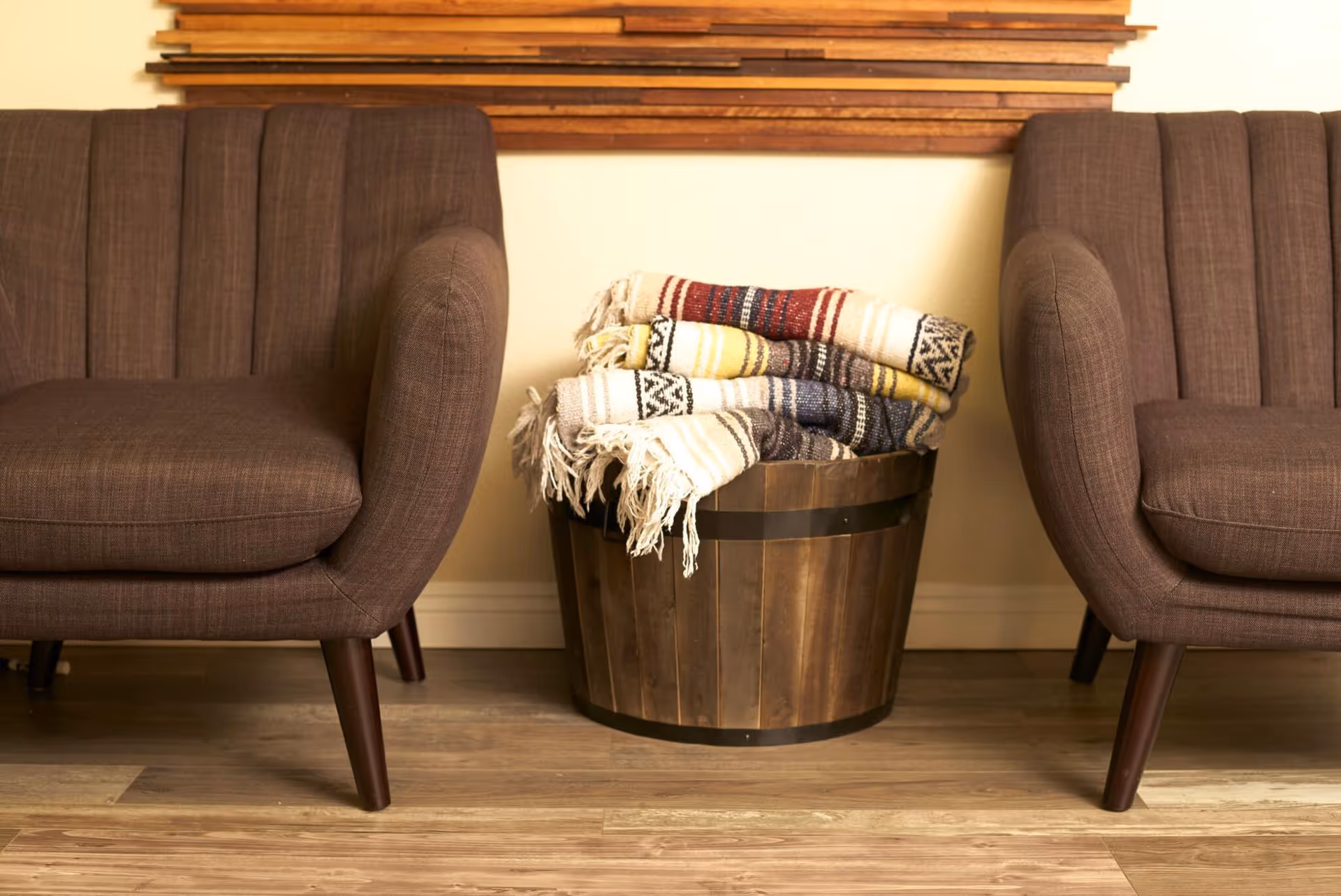 Two brown chairs frame a wooden bucket with folded blankets in a cozy living room.
