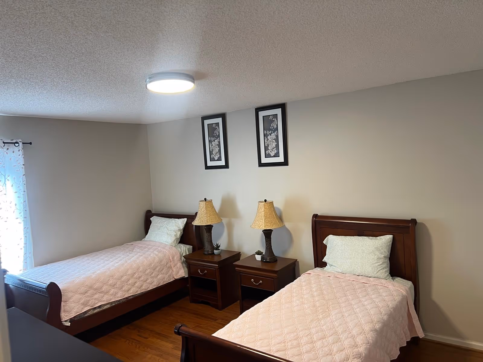 Two single beds with matching wooden frames, bedside tables, and lamps in a bright bedroom.