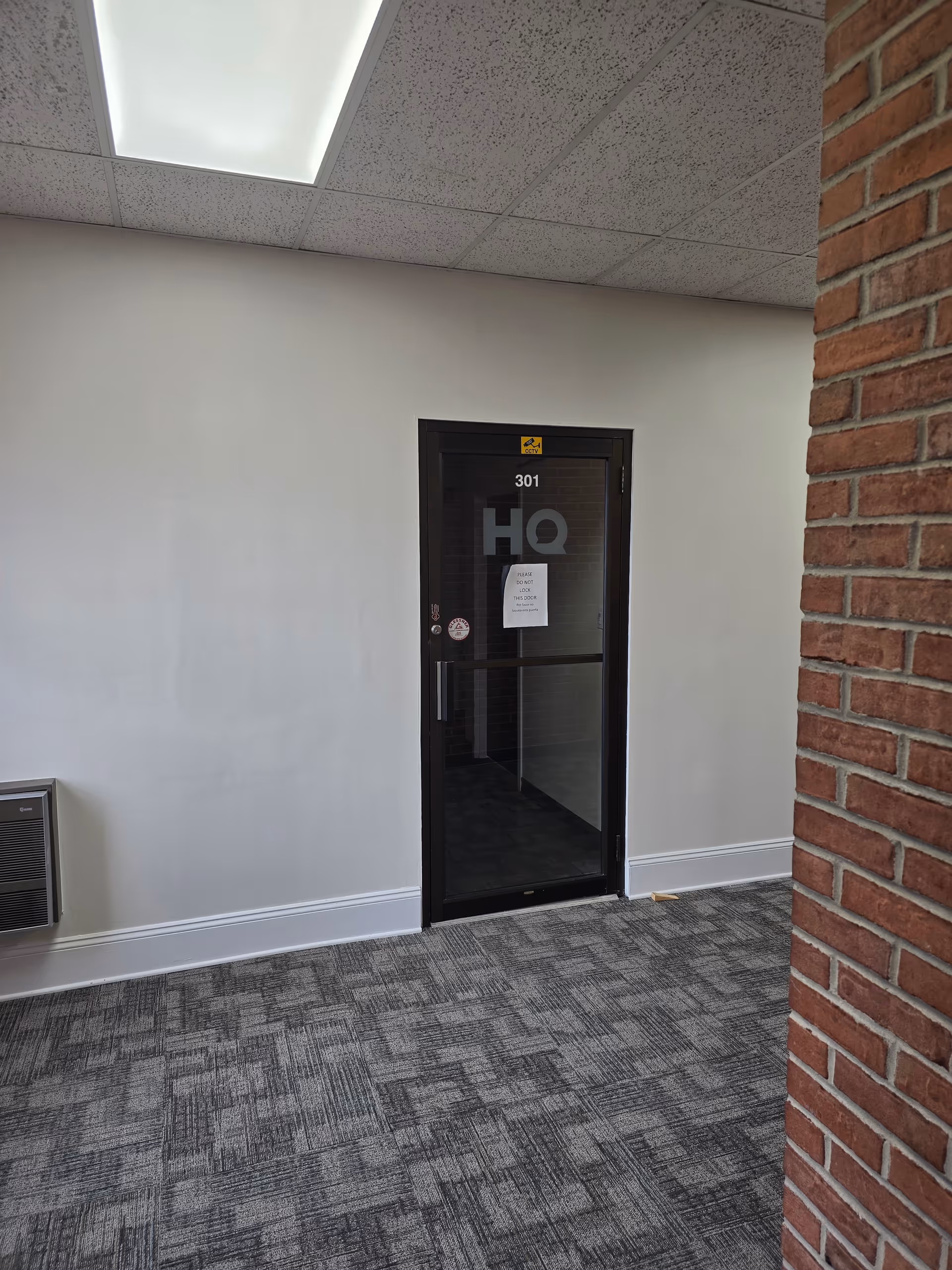 Interior hallway featuring a glass door labeled 301 HQ beside a brick wall.