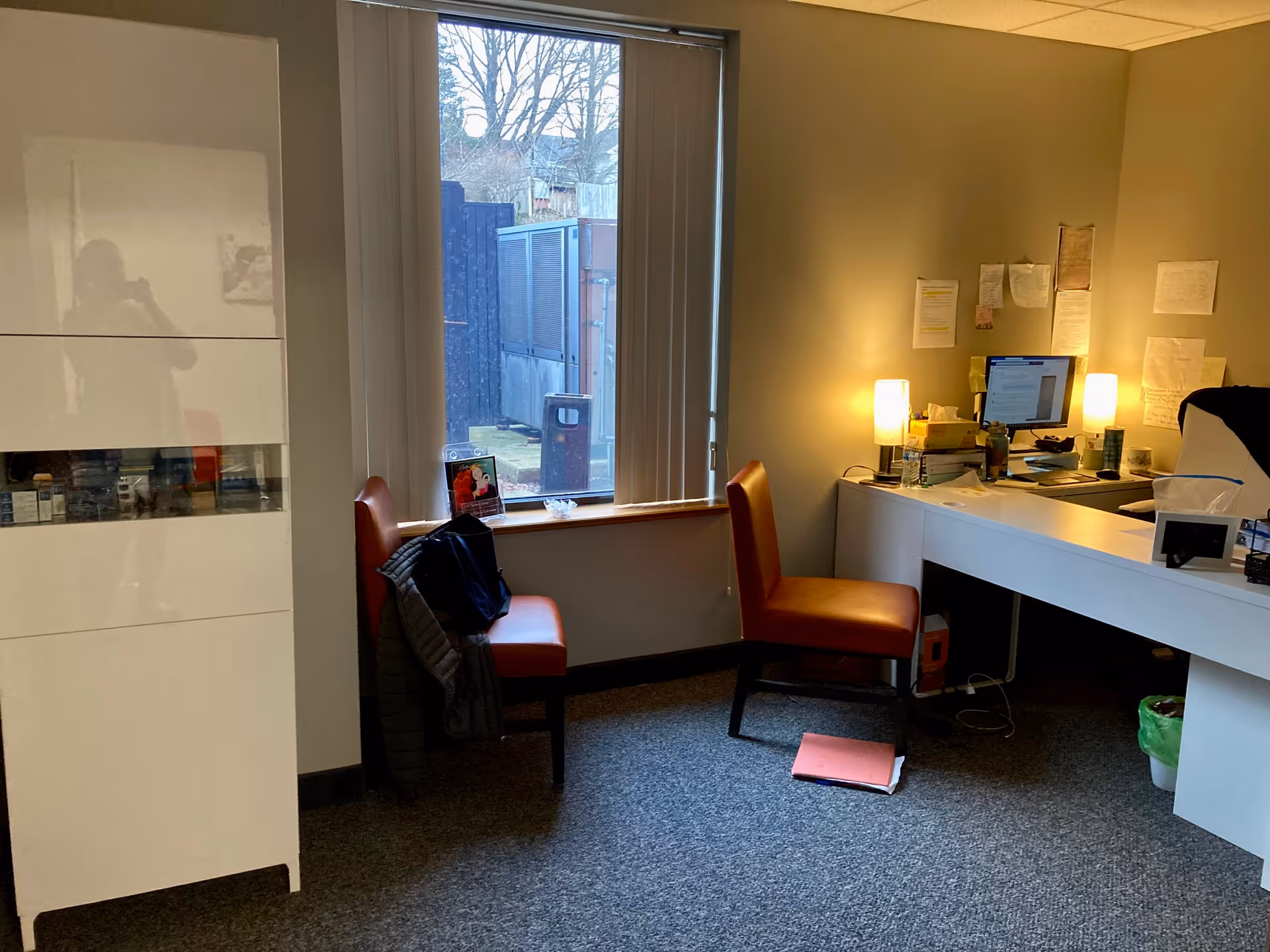 Office workspace with a white desk, red chairs, computer, and bulletin boards.