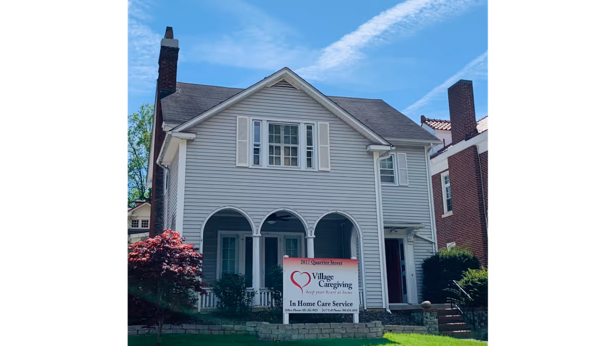 Front view of a two-story gray house with arched porch and Village Caregiving sign.