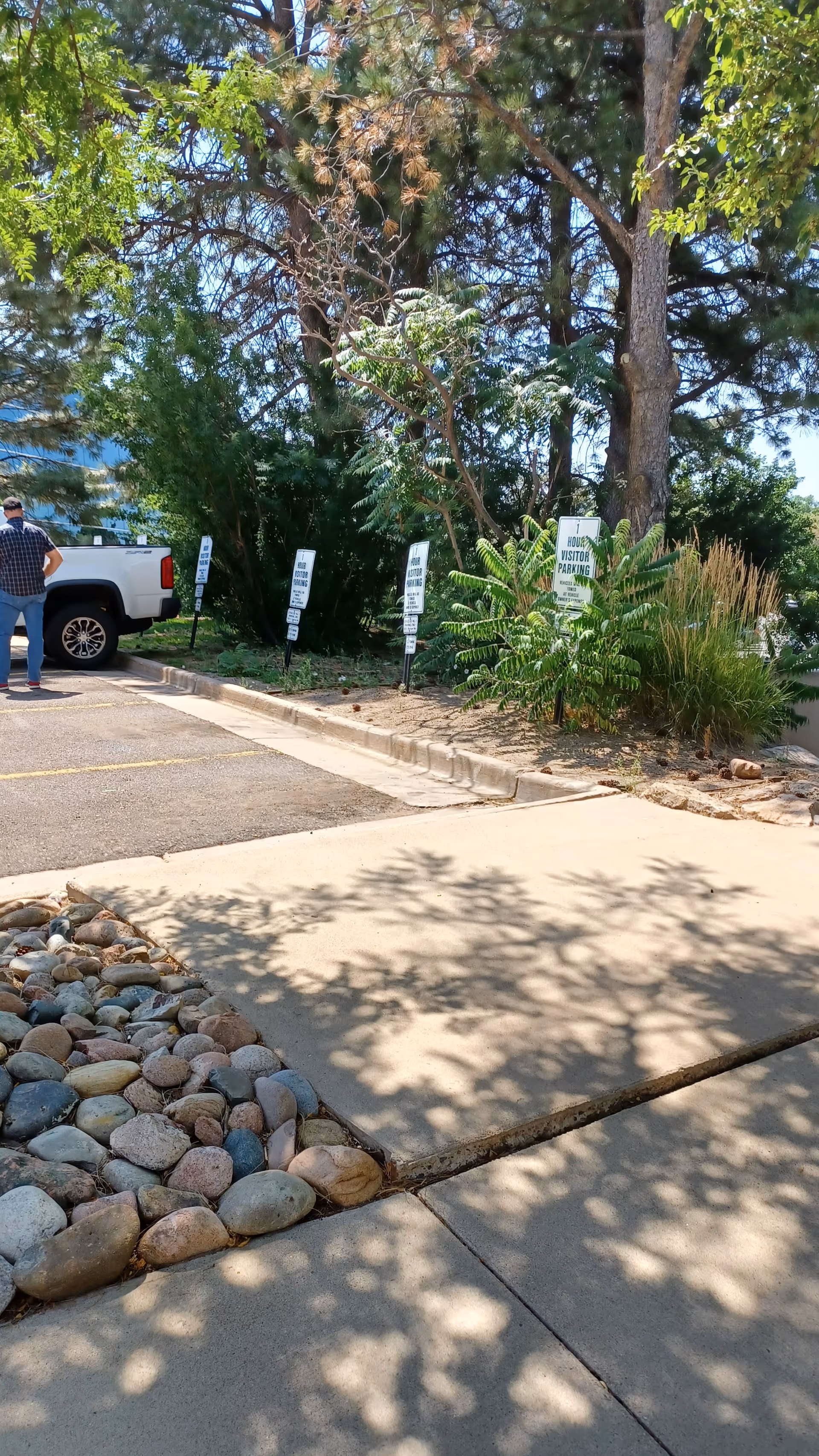 Outdoor parking area in front of building with trees, signs, and a person near a truck.