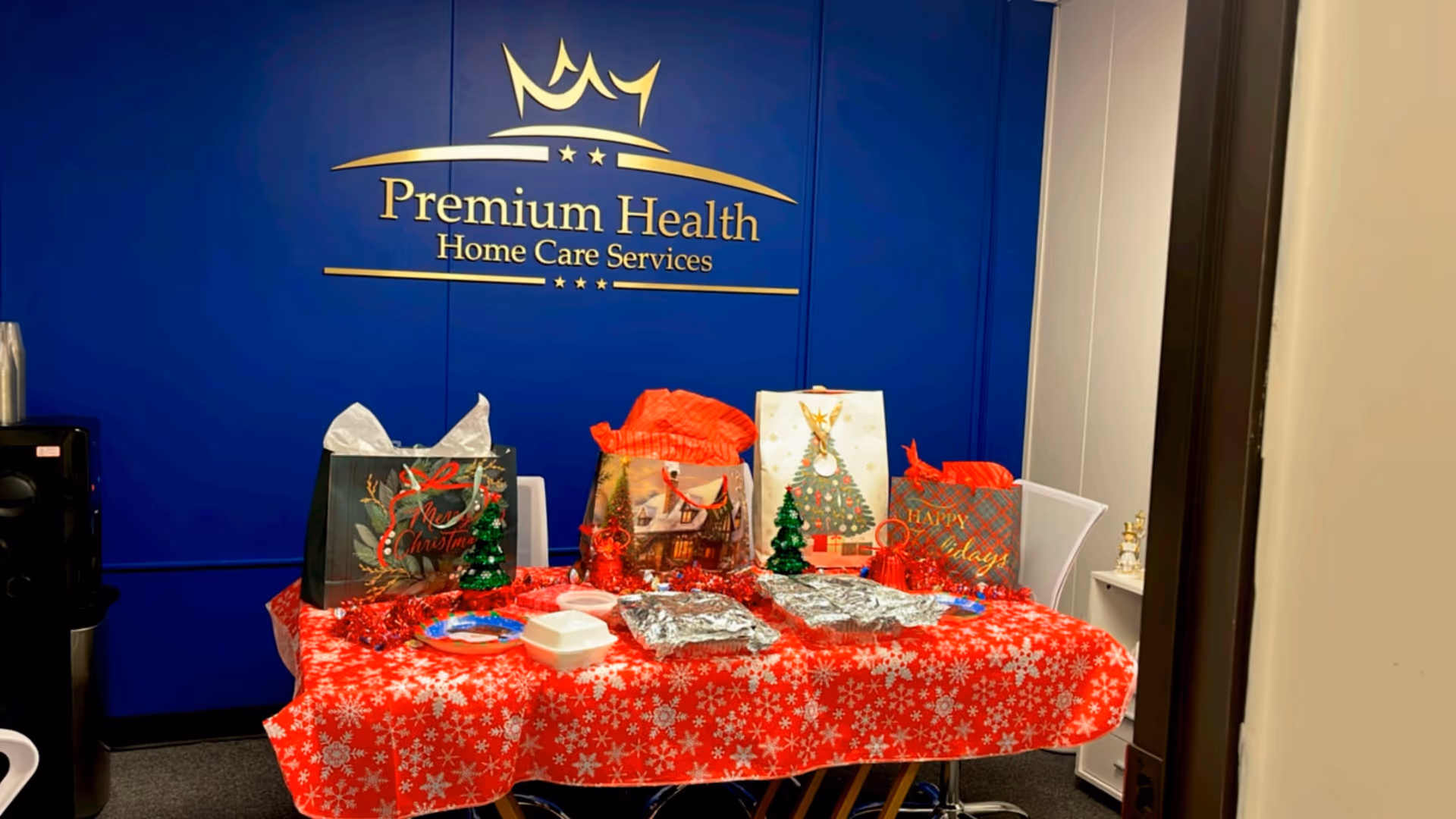 Blue wall with Premium Health Home Care Services logo behind a red holiday gift table.