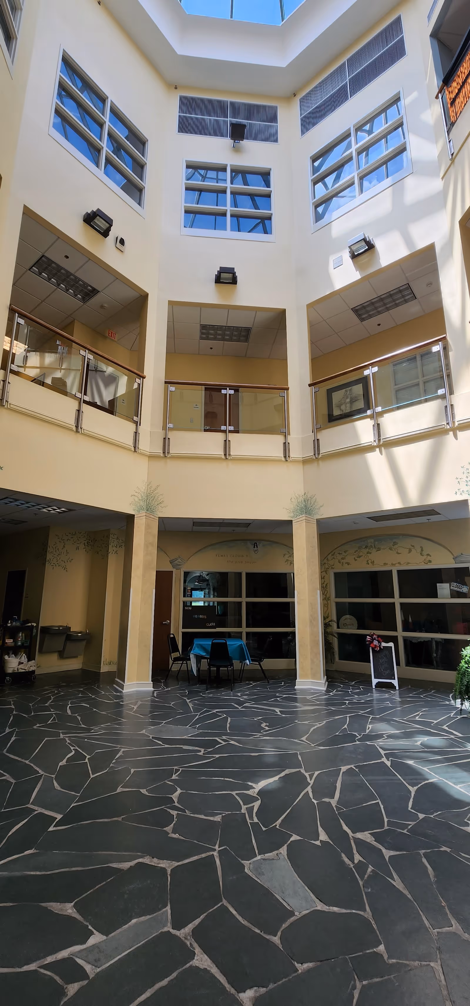 Bright three-story interior atrium with glass balconies, skylights, and a seating area on the ground floor.