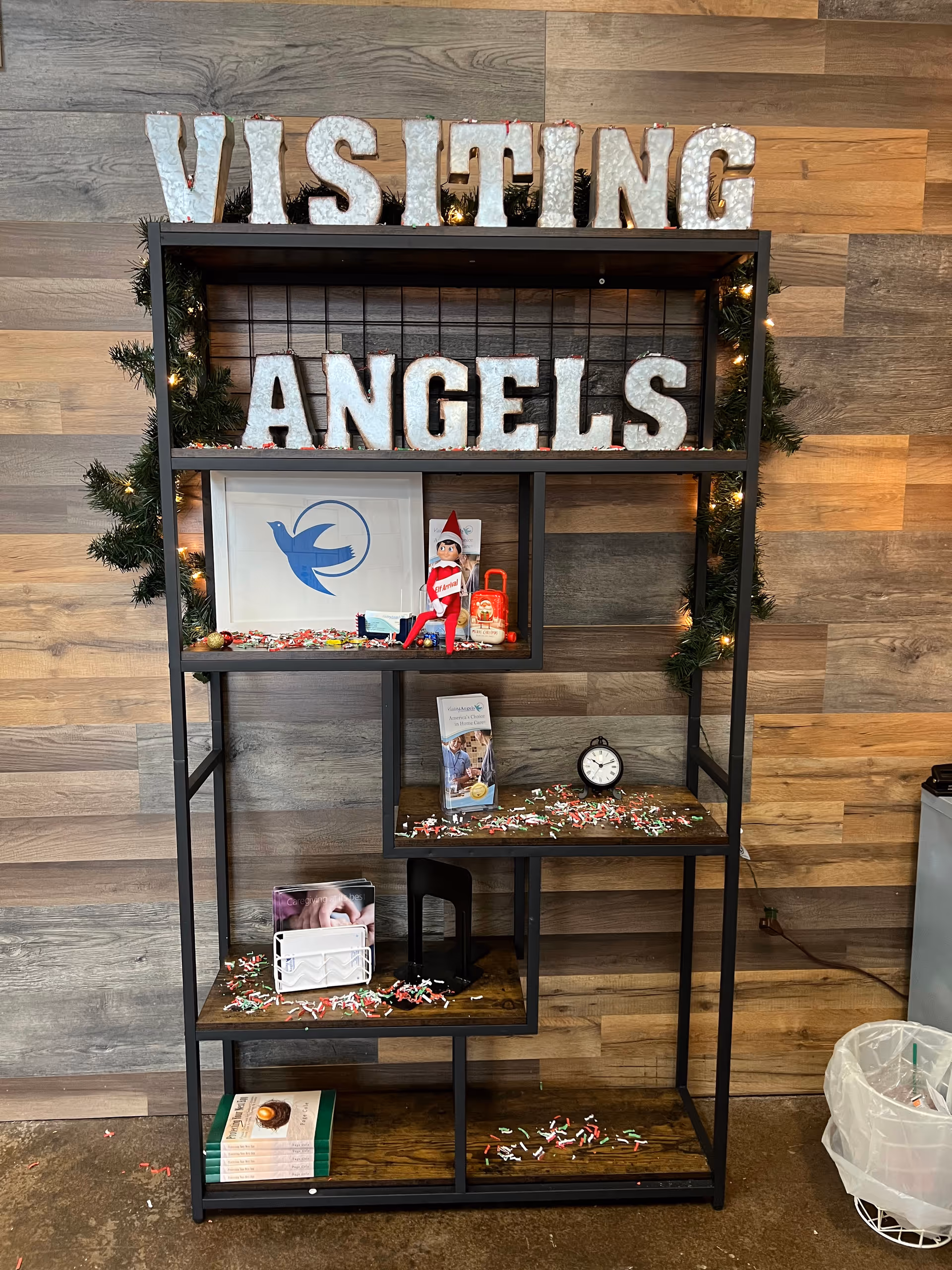 Interior display shelf with visiting angels signage and holiday decorations in a warm wood backdrop.