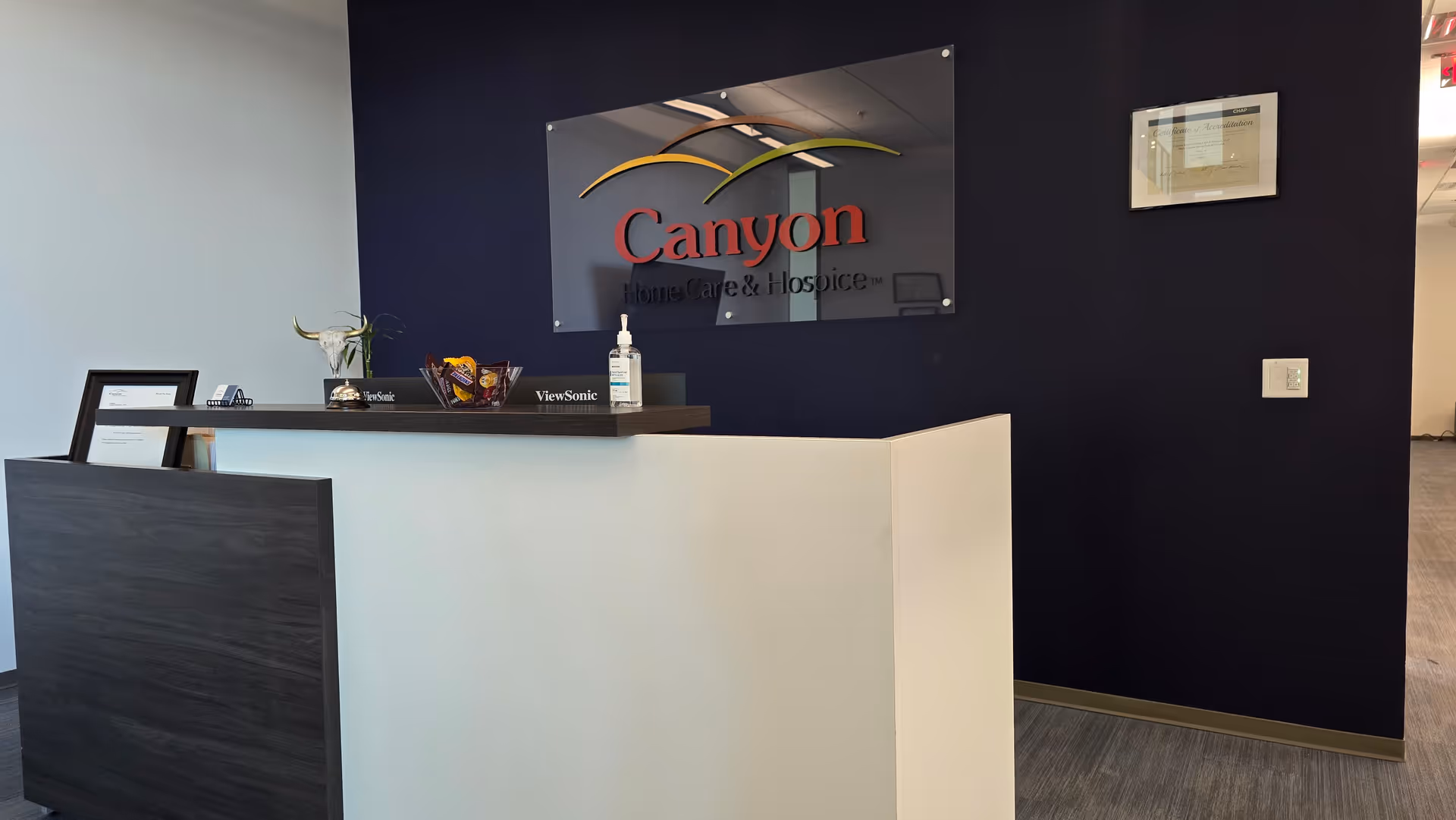 Reception desk in a modern lobby with Canyon Home Care & Hospice sign on navy wall.