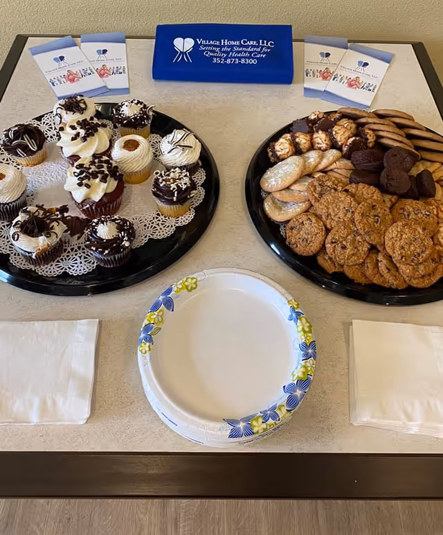 Dessert trays with cupcakes and cookies on a counter beside a Village Home Care sign.