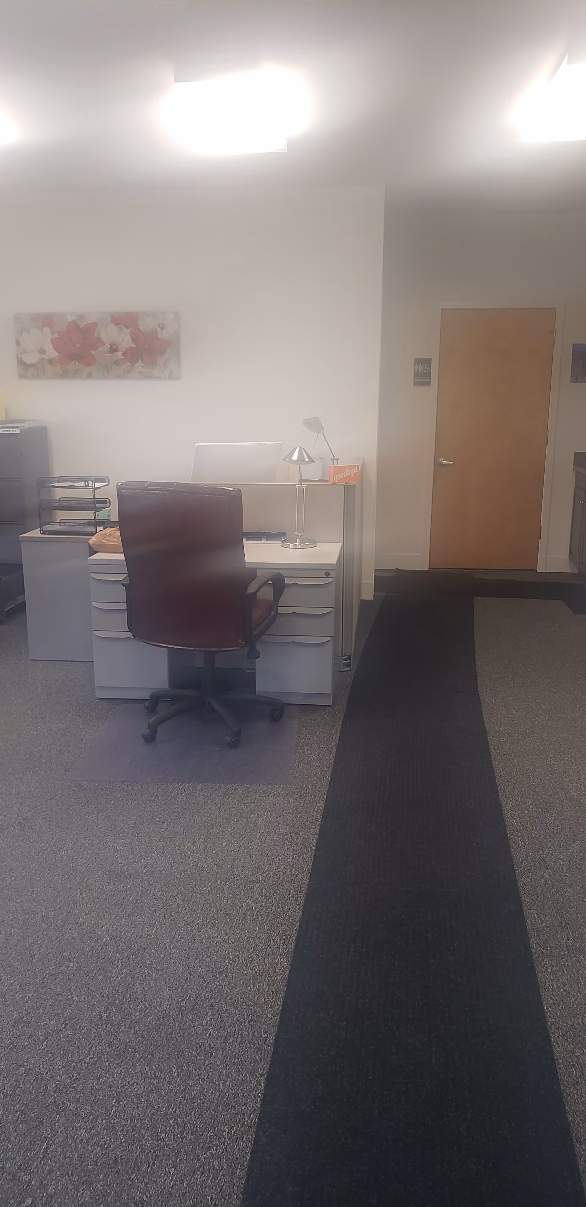 Office workspace with desk, maroon chair, lamp, and file trays in a facility.