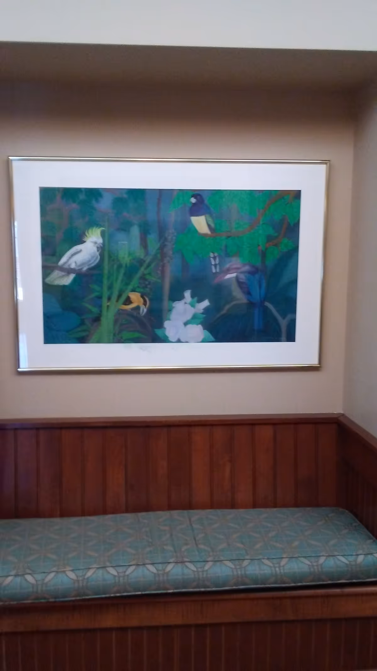 Framed colorful bird artwork on beige wall above a wood-paneled bench with a patterned cushion