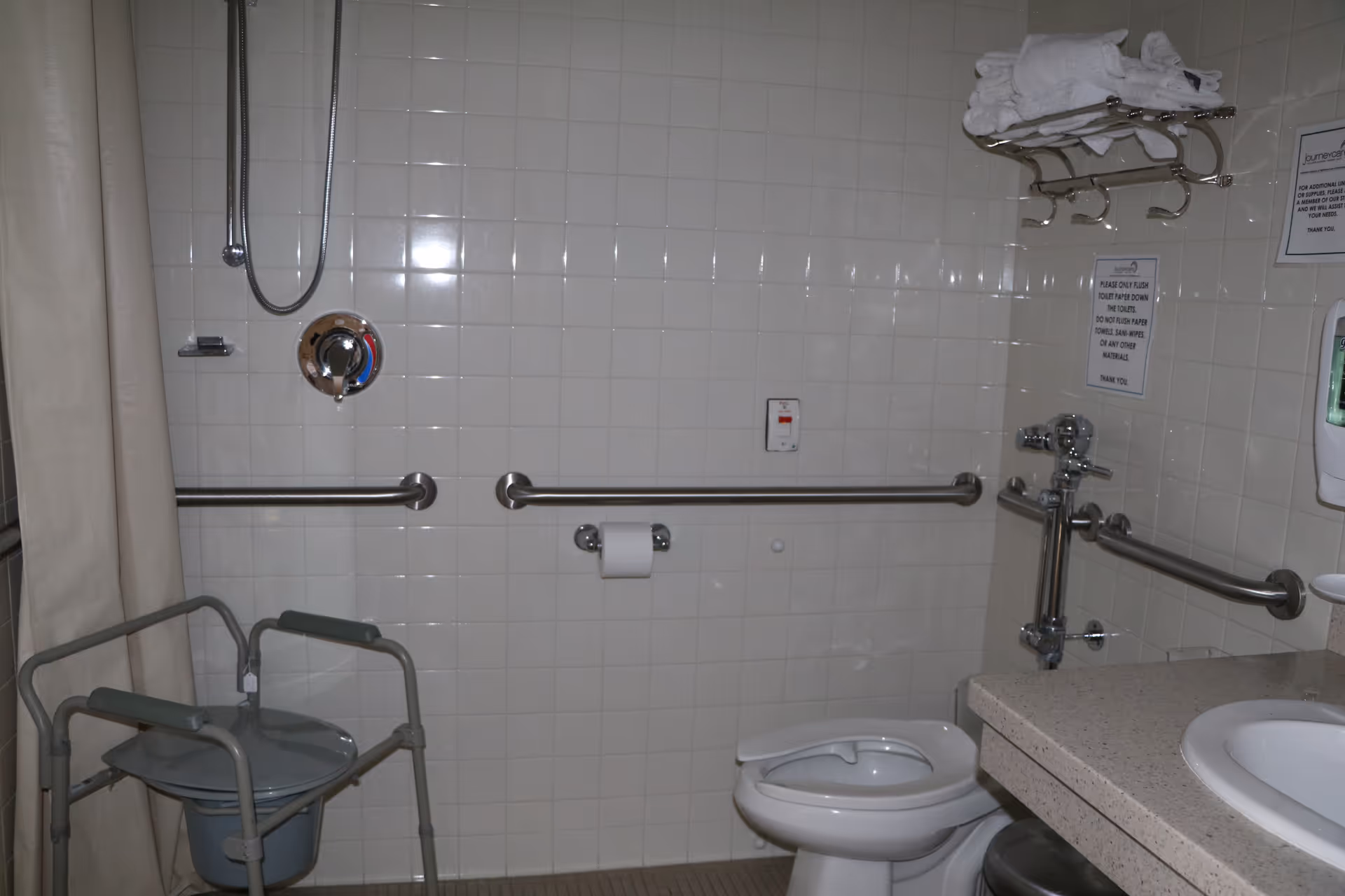Accessible bathroom with grab bars, shower, toilet, sink, and a shower chair.