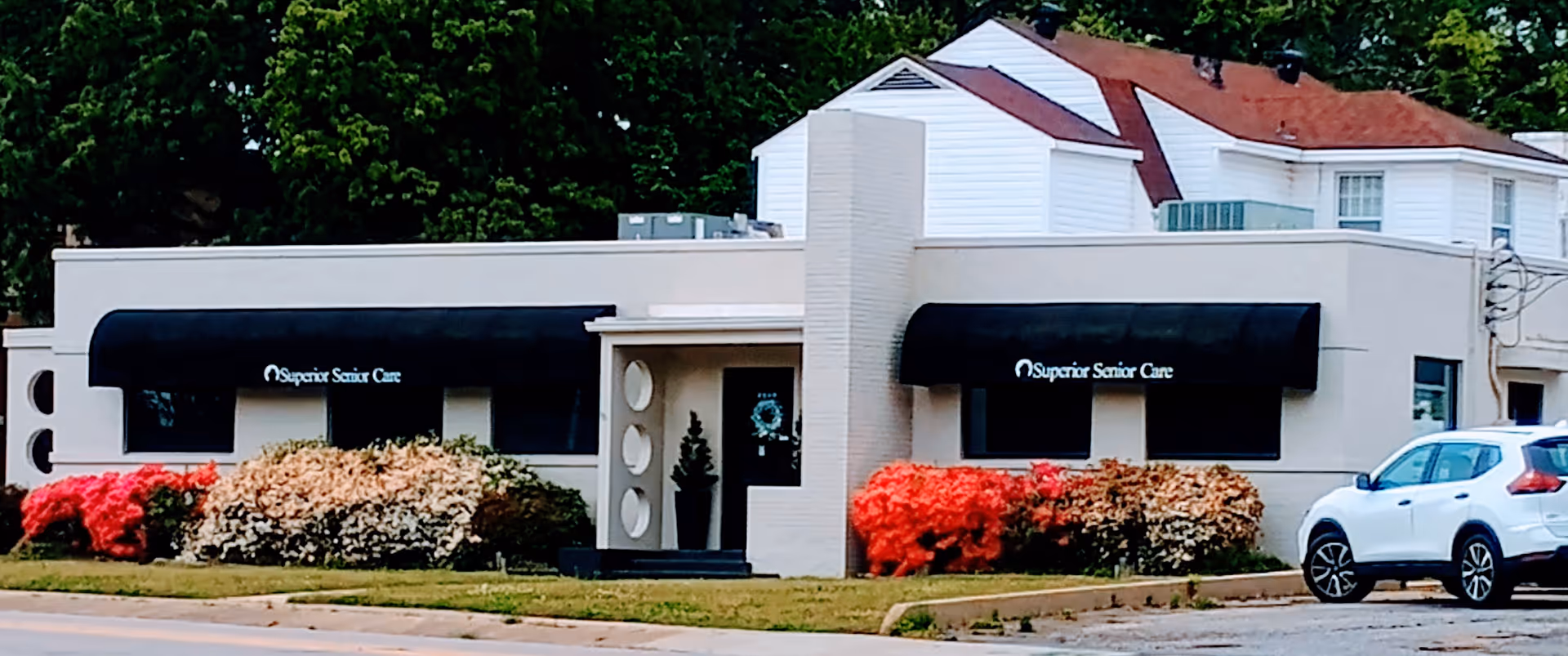 Exterior view of Superior Senior Care facility with black awnings, shrubs, and a parked white SUV.
