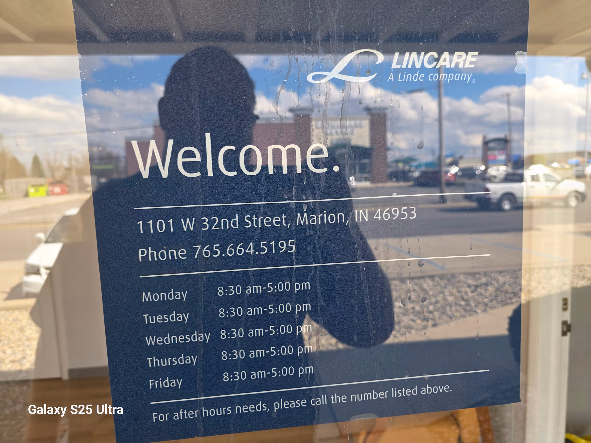 Glass door with a Welcome sign from LINCARE, reflecting a parking lot and photographer.