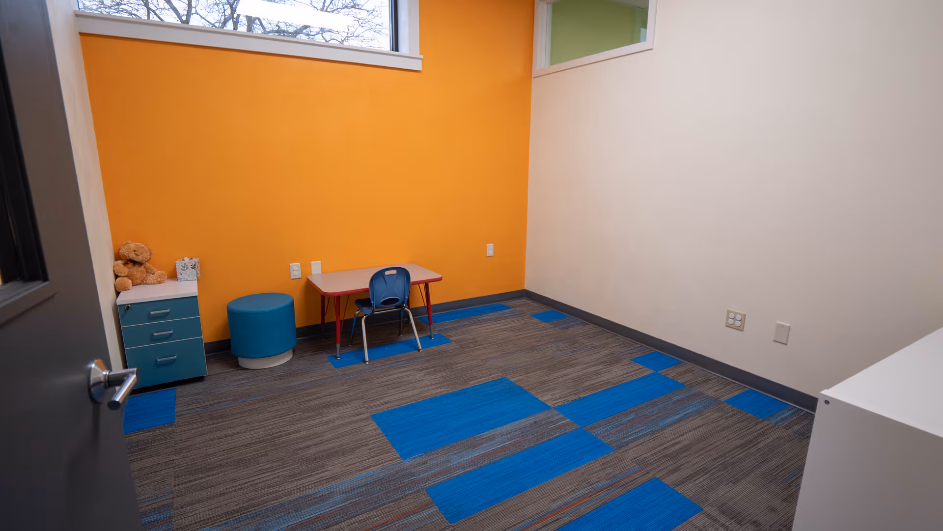 Colorful interior room with small table, chair, toy storage, and orange accent wall.