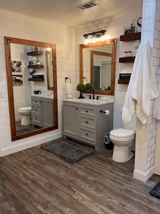 Bathroom with dual sinks, wood-framed mirrors, towel racks, and shelves.