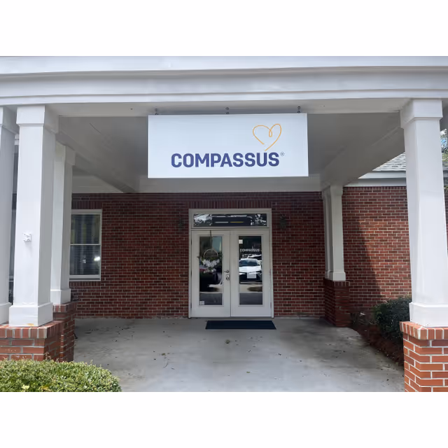 Brick building entrance with a white Compassus sign under a covered porch.