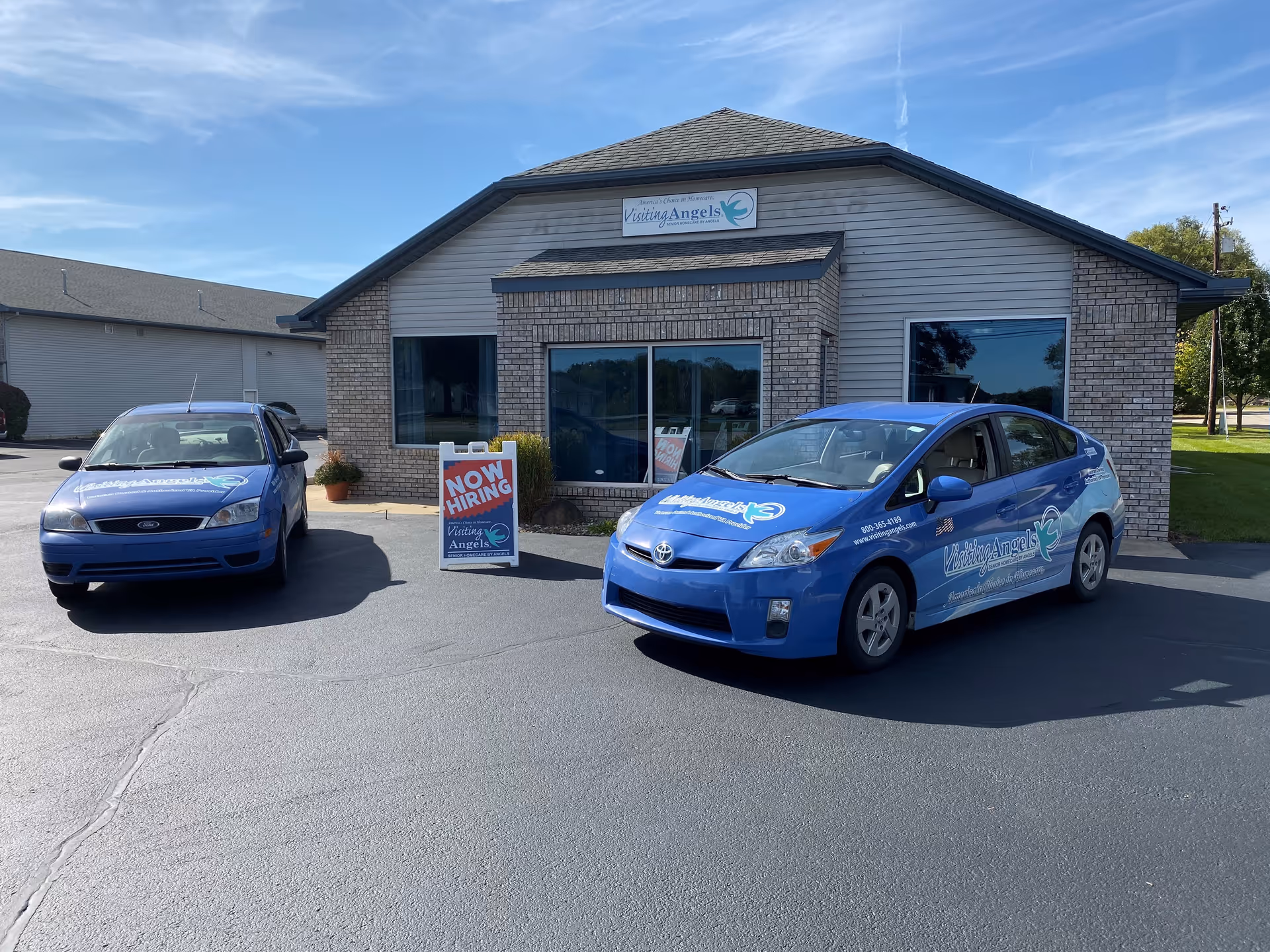 Front view of Visiting Angels Senior Home Care building with two blue company cars parked outside.