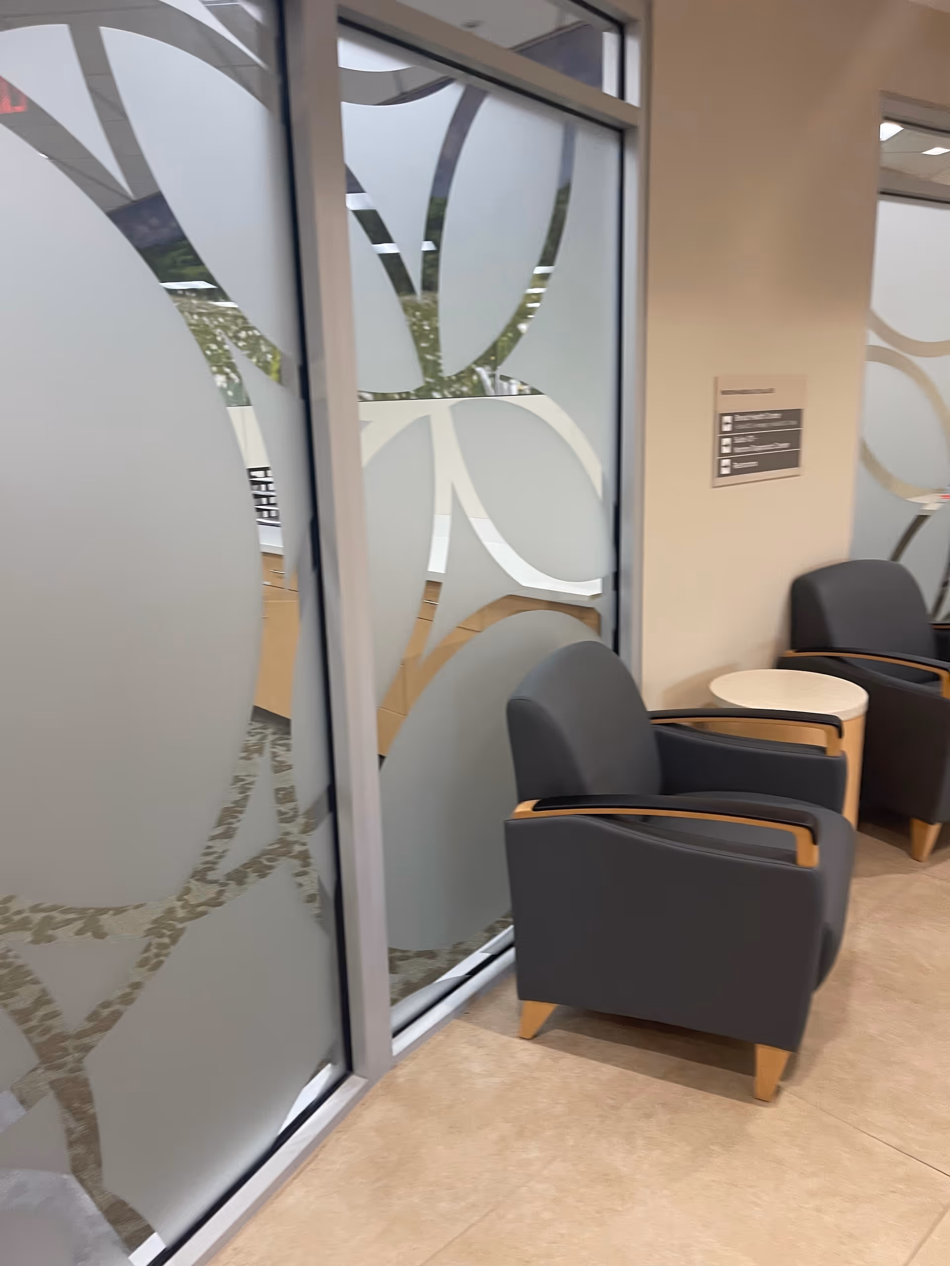 Indoor waiting area with frosted glass partitions and gray wooden-armrest lounge chairs.