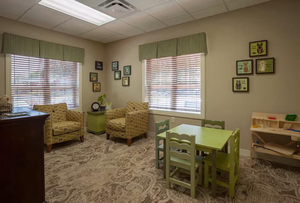 Bright senior living area with two patterned chairs, a small green kid-sized table, and wall art.
