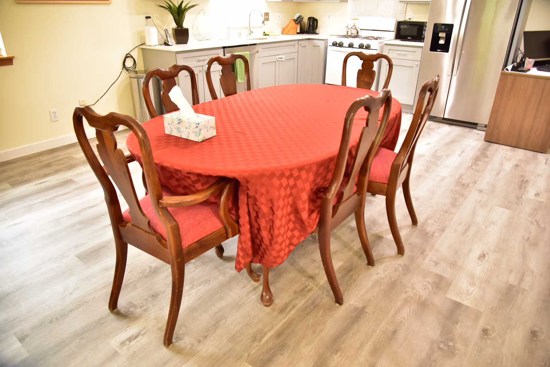 Red checkered dining table with six wooden chairs in a bright kitchen.