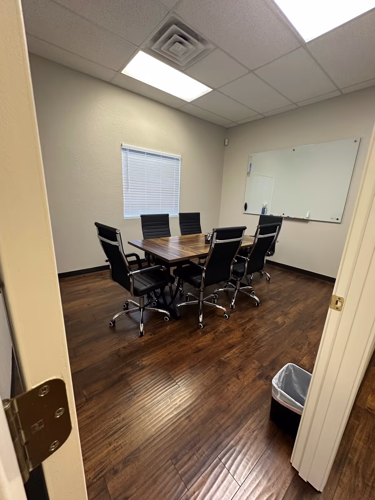A small conference room with a table, several chairs, whiteboard, and wood flooring.