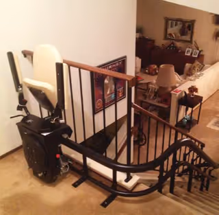 A stairlift chair runs along a stair railing inside a residential interior.