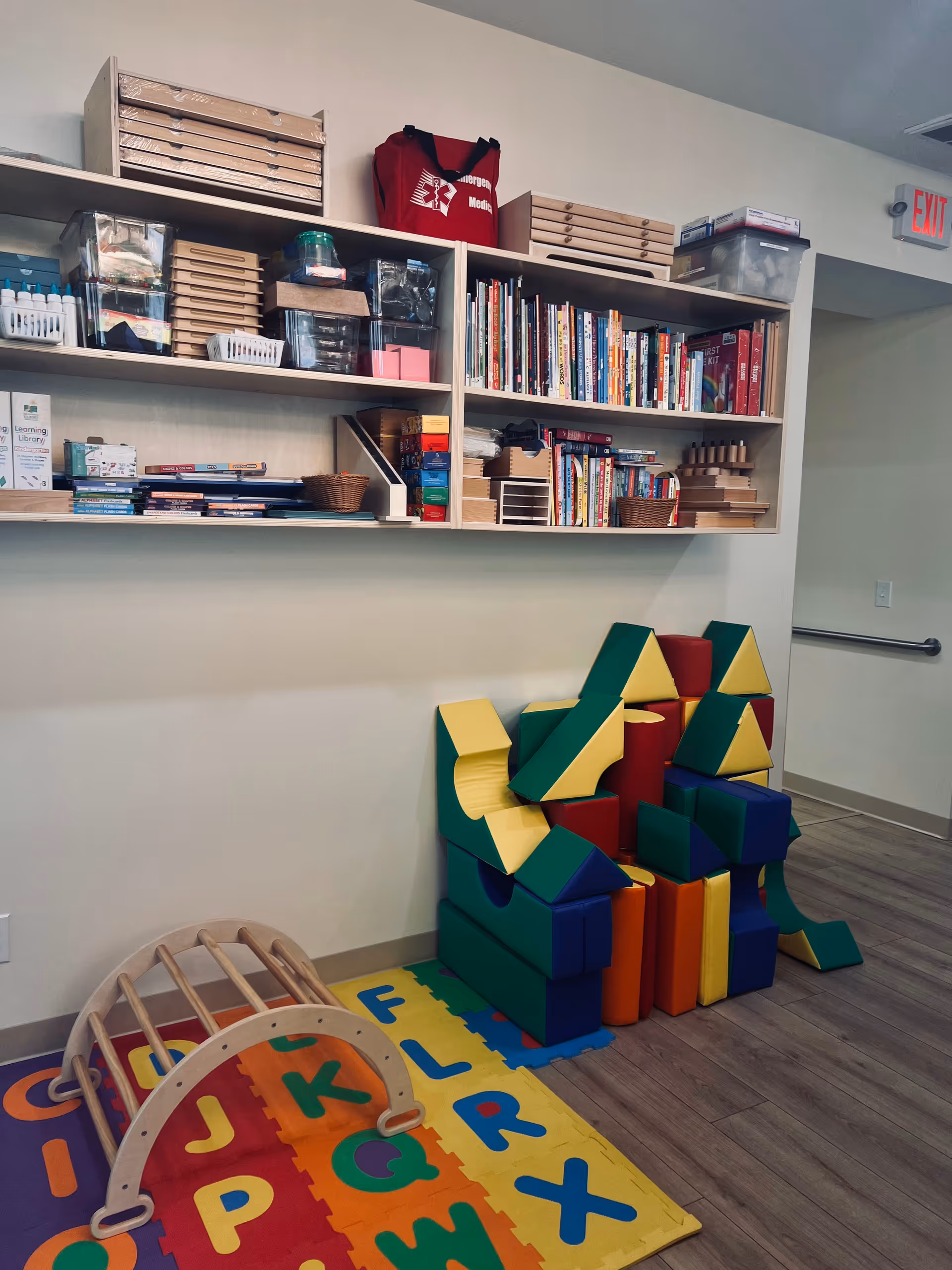 Indoor activity room with shelves, colorful foam blocks, and alphabet mats.