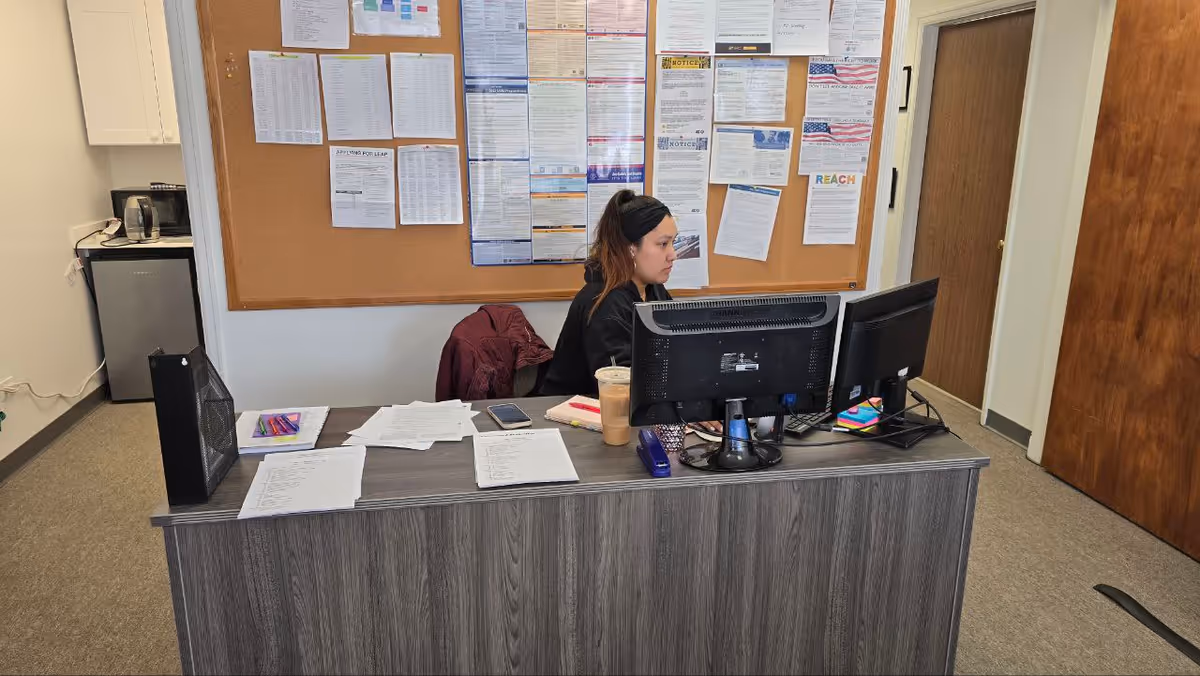 Staff member sits at a desk with computer in an office with bulletin boards