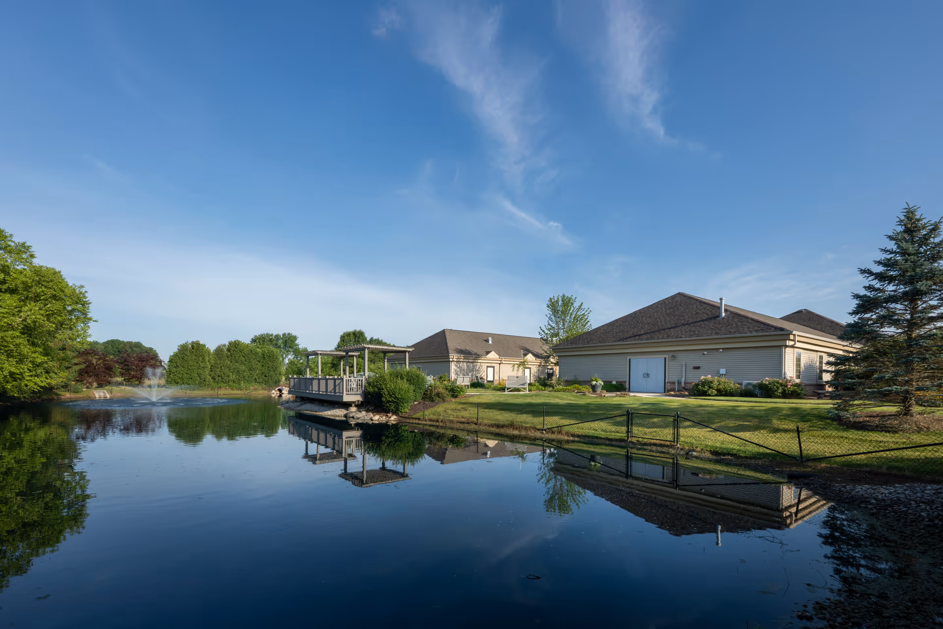 Exterior view of a Stillwater Hospice IN facility beside a pond with a dock and lawn.