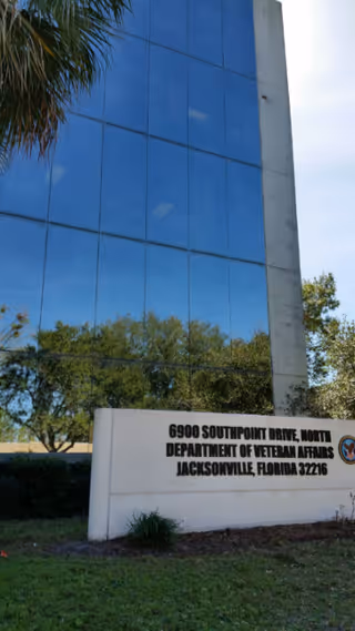 Exterior view of a glass-front building with a sign and trees.