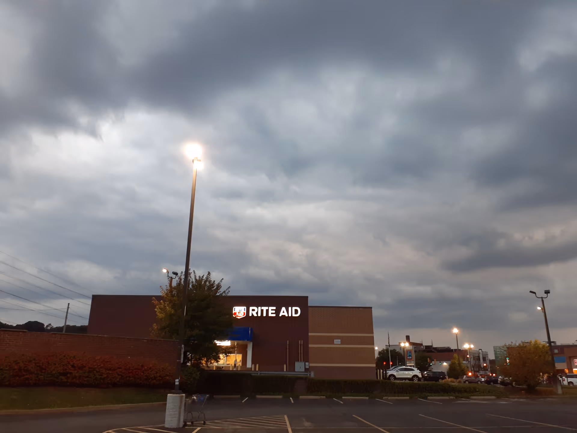Exterior view of a Rite Aid store at dusk with parking lot and cloudy sky.