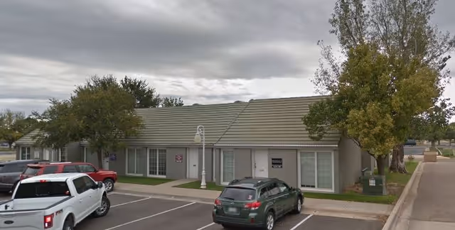 Exterior view of CNS Cares senior living facility with parked cars and trees
