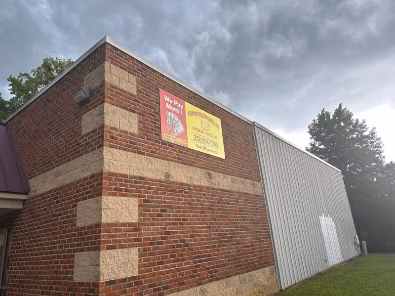 Brick building exterior with a yellow sign on the wall and metal siding nearby.