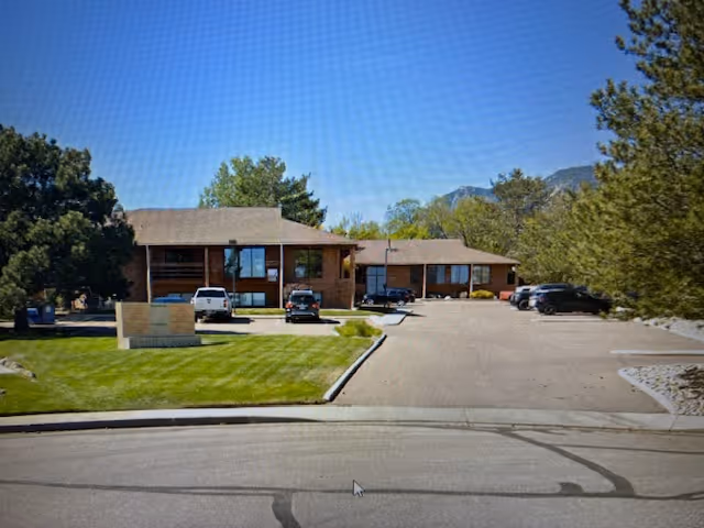 A single-story Comfort Keepers Home Care building with a parking lot, trees, and distant mountains.