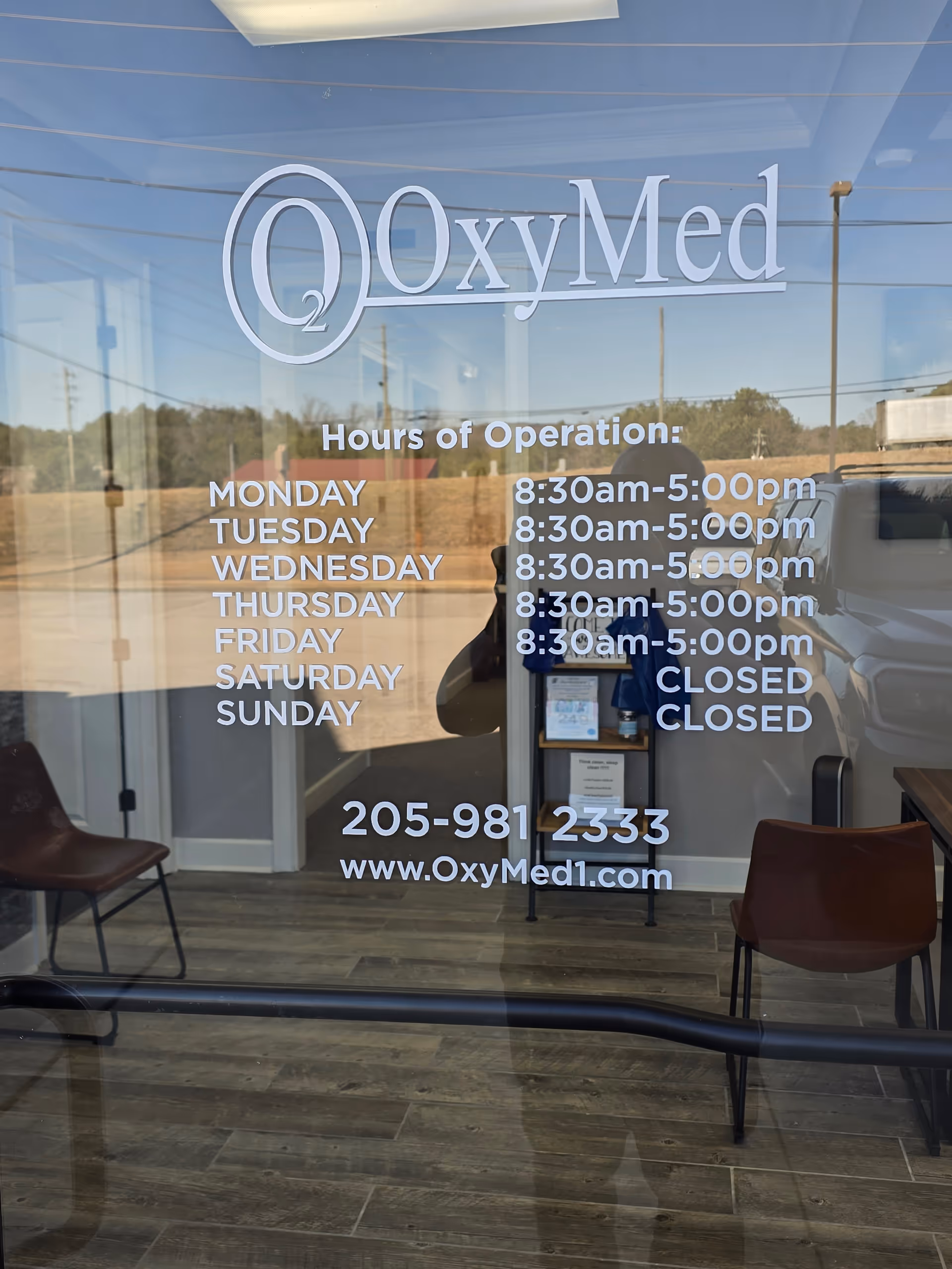 Glass door displays OxyMed logo, hours, contact info, and a small waiting area.