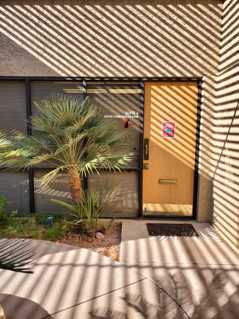 Exterior view of the Aspire Home Healthcare building entrance with a door, blinds, and palm plants.