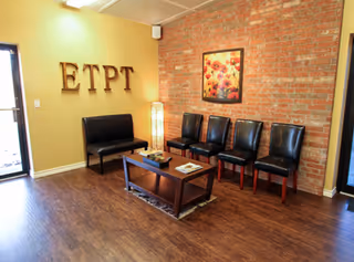A waiting area with brick accent wall, row of black chairs, and ETPT letters.
